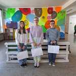 Troje laureatów konkursu stojących na tle szkolnej ściany z nagrodami w rękach.jpg