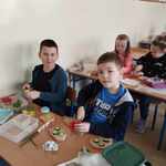 Uśmiechnięci  chłopcy siedzący przy stolikach w klasie wykonują zdrowe kanapki.jpg