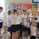 Grupa dzieci podnosi do góry ręce z pucharem za zdobycie pierwszego miejsca.