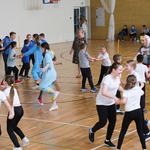 Grupa uśmiechniętych dzieci tańczących w kółkach na sali gimnastycznej.