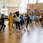 Grupy dzieci tańczą na sali gimnastycznej.