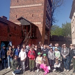 Grupa uczniów pozuje do zdjęcia na tle średniowiecznych murów w Toruniu.
