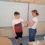 Pani pielęgniarka pokazuje sposób opatrywania łokcia bandażując łokieć uczniowi.