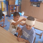 Dwóch uczniów ćwiczy opatrywanie głowy za pomocą bandaża.