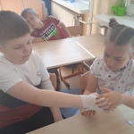 Grupa uczniów ćwiczy opatrywanie ręki za pomocą bandaża.