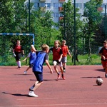 Grupa chłopców w strojach sportowych gra w piłkę nożną na boisku szkolnym.
