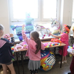 Grupa dziewczynek szykuje się do zdjęcia w fotobudce. Przed nimi kolorowe balony.