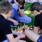 Trzech chłopców gra w szachy siedząc na trawie.
