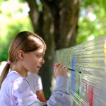 Uczennica maluje farbami na folii spożywczej zawieszonej pomiędzy drzewami.