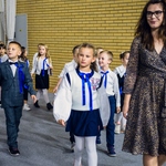 Wychowawczyni klasy 1a wprowadza elegancko ubrane dzieci na salę gimnastyczną.