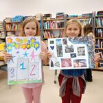 W bibliotece dwie uczennice pozują do zdjęcia z swoimi pracami Mapa marzeń. W tle półki z książkami..jpg