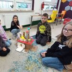 9 Uczniowie siedzą na dywanie i pozują do zdjęcia z wykonaną przez siebie budowlą zrobioną z kartoników i rolek po papierze..jpg