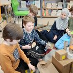 12 Uczniowie siedzą na dywanie i tworzą budowle z kartoników_ rolek po papierze. W tle półka z książkami i kolorowe krzesła..jpg