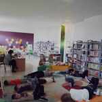 Nauczycielka biblioteki czyta bajkę terapeutyczną dzieciom leżącym na podłodze w bibliotece szkolnej.jpg