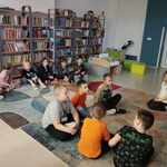 Uczniowie siedzący na podłodze w bibliotece szkolnej słuchają czytanej bajki.jpg