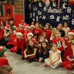 Świątecznie ubrane dzieci siedzą w oczekiwaniu na przybycie Świętego Mikołaja. W tle dekoracyjny kominek..jpg