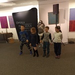 Dzieci stoją na tle plakatu opery i odpowiadają na pytania prowadzącej.jpg