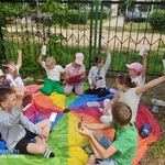Grupa dzieci siedzi na kolorowej chuście  i wykonuje zadania konkursowe..jpg