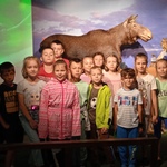 Dzieci pozują do zdjęcia w muzeum przyrodniczym, w tle widoczny jest łoś.