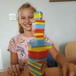 uczennica siedzi w lawce_ usmiecha sie_ pokazuje zbudowana wieze z figur geometrycznych.jpg